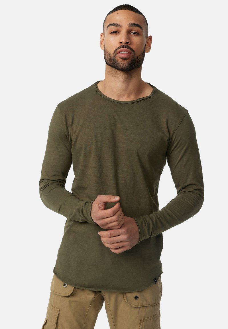Langärmliges olivgrünes Shirt mit rundem Ausschnitt und weicher Textur, entworfen mit einer figurbetonten Silhouette und leicht ausgefranstem Saum.