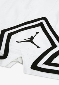 White perforated fabric shorts feature black accents and a prominent black Jumpman logo on the lower side, outlined in contrasting stitching.