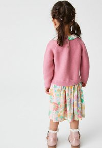 Vaaleanpunainen neulepaita, jossa on ribattu helma, kukallinen hame pastelinvärisissä sävyissä ja vaaleanpunaiset saappaat, joissa on valkoinen turkisreunus ja koristeellinen metalliosuus.