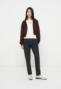 Burgundy cropped hoodie over a white shirt, paired with dark grey jeans and light grey slip-on shoes. Simple design, relaxed fit, no patterns.