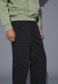 Zwarte cargobroek met zijzakken, gecombineerd met een lichtgroene hoodie. De stoffen zijn soepel en hebben een lichte textuur, met ribgebreide boorden.