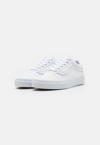 White sneakers with a textured design. Features a low profile, smooth canvas upper, lacing system, and a flat rubber sole. Accented with subtle patterns.