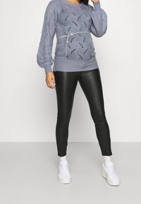 Suéter de punto azul claro con diseño de calados, puños y dobladillo acanalados. Combinado con leggins de piel sintética negra y zapatillas blancas.