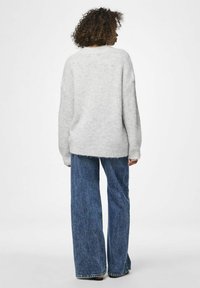 Šviesiai pilkas per didelis megztinis su žemomis pečių siūlėmis, megztu tekstūru ir gumbinėmis rankovėmis, derintas su plačiomis džinsinėmis kelnėmis.