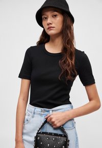 Černé tričko s krátkým rukávem a kulatým výstřihem, v kombinaci s světle modrými džínovými šortkami a malou černou kabelkou se cvočky. Texturovaný černý klobouk.