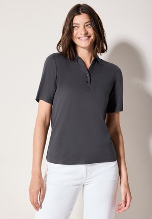 Donkergrijze polo met korte mouwen, voorzien van een knoopsluiting en een zachte textuur, gecombineerd met witte broek. Eenvoudig ontwerp en een klassieke pasvorm.