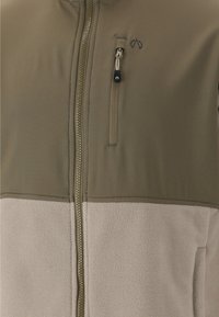 Lettejakke med tofarvet design, hvor den øverste del er olivengrøn, og den nederste del er beige fleece. Fuldt frontlynlås, justerbar krave.