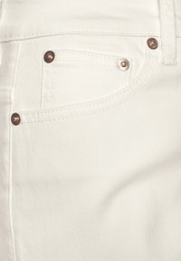 Jean en denim blanc avec des rivets couleur cuivre, design cinq poches, couture visible et un tissu doux légèrement texturé.