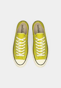 Sneakers verzi din canvas cu sireturi albe, vârf rotund și talpă din cauciuc negru contrastant. Căptușeala interioară este de culoare crem cu branding.