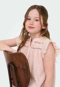 Ljusrosa blus med volangärmar, spetsdetaljer och vertikala ränder. En trästol med böjd ryggstöd syns i bilden.