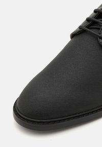 Black leather dress shoe with a textured surface, rounded toe, and lace-up design. Features a smooth sole with stitching accents.