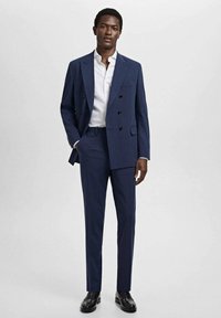 Marineblauwe dubbelknopen kostuum met een notched lapel, gecombineerd met een wit overhemd en zwarte leren schoenen, met een gladde stof en een op maat gemaakte pasvorm.