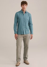 Camisa de manga larga turquesa con cuello abotonado, combinada con pantalones beige claros y zapatos marrones claros, con un tejido suave y un corte relajado.