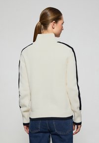 Stickad tröja i krämfärg med hög krage, med svarta sidostripes och ribbad nederkant och ärmar. Texturerat tyg med en boxig passform.