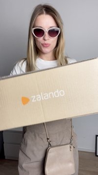 Brown corrugated cardboard box labeled with "zalando" in white font, held in front of a person wearing purple-tinted cat-eye sunglasses.