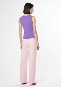 Top viola senza maniche abbinato a pantaloni larghi rosa chiaro. Il top ha un design aderente, mentre i pantaloni presentano un vita alta e cuciture visibili.