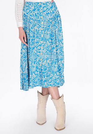 Sininen midihame valkoisella kukkakuviolla ja edessä napit, yhdistetty beigenvärisiin cowboy-saappaisiin ja valkoiseen silkkipuseroon, jossa on reikäkukkaiset hihat.