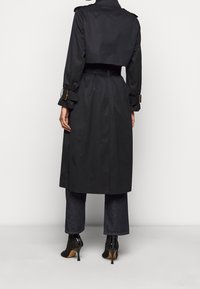 Czarny płaszcz o skróconym kroju, z paskiem w talii, naramiennikami i akcentami w postaci pasków. W połączeniu z ciemnymi dżinsami i wysokimi obcasami.