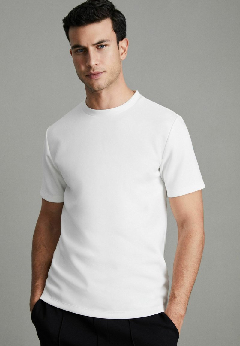 Camiseta blanca de manga corta con escote redondeado, confeccionada en tejido suave. Presenta un diseño sencillo y un corte relajado.