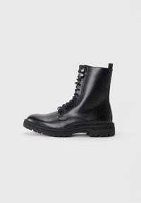 Botas de combate de cuero negro con cordones, punta redonda, acabado texturizado y suela de goma gruesa con surcos profundos. Asa en la parte posterior.