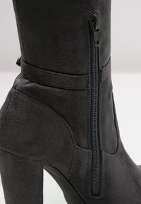 Bota de tobillo de ante negro con una textura suave, que cuenta con una cremallera lateral, tacón cuadrado y un diseño minimalista.