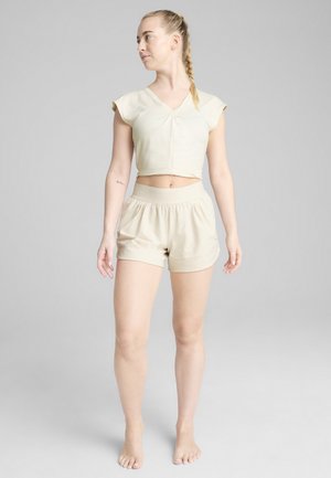 Beige cropped top with short sleeves and a v-neck, paired with matching elastic waist shorts. Smooth fabric with a relaxed fit.