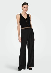 Débardeur noir à côtes avec des détails de boutons, associé à un pantalon large noir taille haute et une ceinture marron. Des ballerines noires complètent le look.