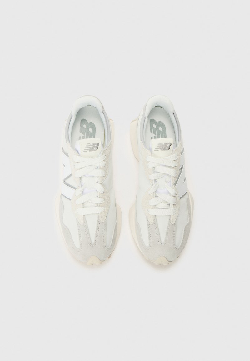 Baskets de sport blanches en cuir lisse et en daim, avec des lacets, une semelle rembourrée et un logo discret sur le côté.
