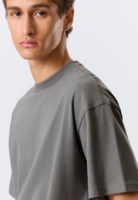 Γκρι βαμβακερό T-shirt με στρογγυλή λαιμόκοψη, κοντά μανίκια και λεία υφή, που παρουσιάζει μινιμαλιστικό σχέδιο και άνετη εφαρμογή.