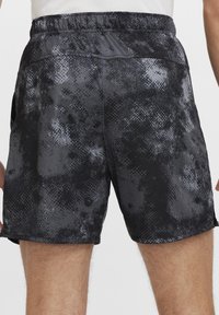 Juodos ir pilkos raštuotos šortai su elastingu juosmeniu, pasižymintys tekstūruota medžiaga ir šoninėmis kišenėmis. Dizainas apima abstraktų spaudinį.