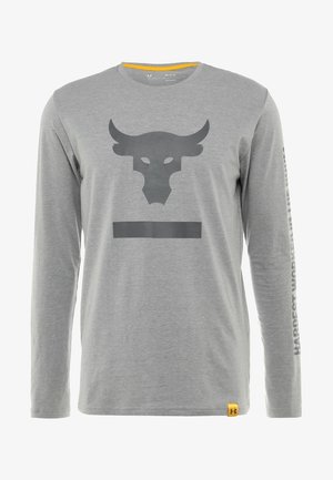 Chemise grise à manches longues avec logo de taureau noir sur la poitrine et texte "Hardest Worker" courant le long de la manche droite. Petite étiquette jaune en bas de l'ourlet.