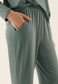 Leichte, weiche grüne Hose mit Gummibund und Seitentasche, die eine glatte Textur und eine lockere Passform bietet.