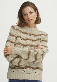Cremfarbener Strickpullover mit strukturierten Mustern, gerippten B�ündchen und hohem Kragen, der braune Wellenakzente aufweist.