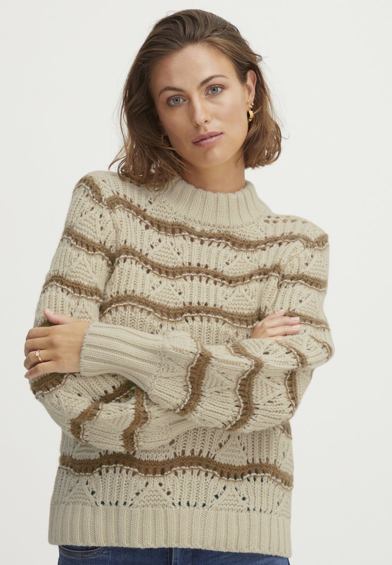 Cremfarbener Strickpullover mit strukturierten Mustern, gerippten Bündchen und hohem Kragen, der braune Wellenakzente aufweist.