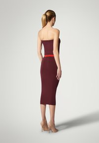 Burgunderfarbene, figurbetonte Midi-Kleid mit einem schulterfreien Design und einem kontrastierenden roten Taillengurt, kombiniert mit hautfarbenen High Heels.