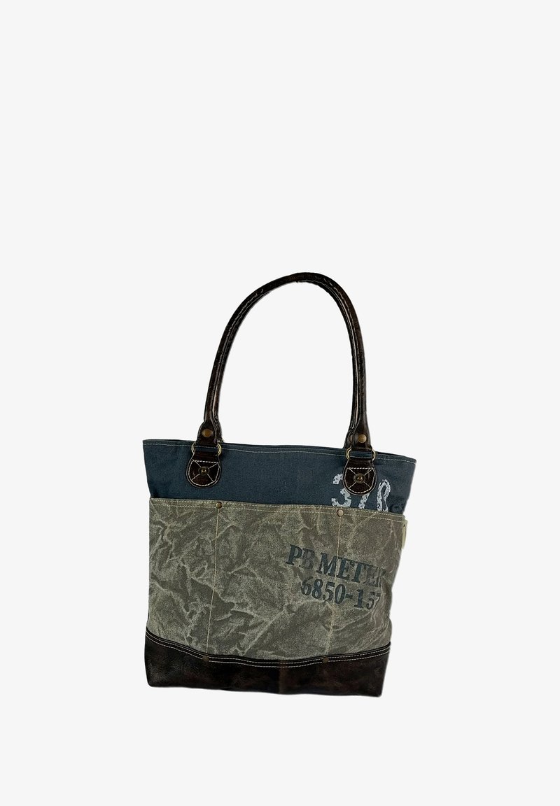 Canvas tas met donkerbruine leren handvatten. Heeft een blauwe bovenkant, een groene onderkant met een patroon en tekstdetails in het zwart.