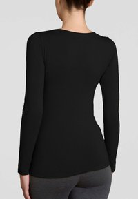 Maglietta nera a maniche lunghe con una texture liscia, design aderente e scollatura arrotondata, abbinata a leggings grigi, che mette in risalto la semplicità.