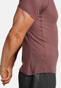 Camicetta attillata a maniche corte in un leggero mauve con un motivo testurizzato a nido d'ape e cuciture visibili, abbinata a pantaloni scuri.