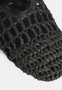 Schwarzer, geflochtener Slip-On-Schuh aus geflochtenem Material, mit einem offenen Strickdesign, runder Zehenform und strukturierten Oberflächen.