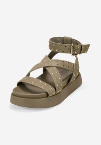 Olive green sandal with crisscross straps featuring gold studs. Thick platform sole, adjustable ankle strap, and textured material.