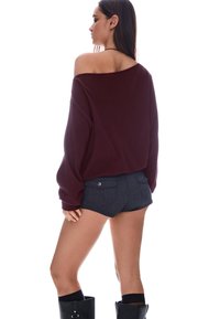 Burgundska oversize pulover z off-shoulder dizajnom, v kombinaciji s temnim jeans kratkimi hlačami z dvema zadnjima žepoma in črnimi visokimi škornji.