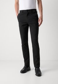 Černé kalhoty s úzkým střihem, vyrobené z hladké látky, s knoflíkovým zapínáním a předními kapsami, doplněné černými mokasínami.