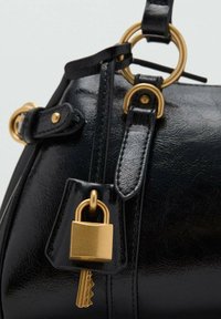 Zwarte leren tas met gouden hardware, voorzien van een hangende gouden hangslot en sleutel, bevestigd aan een leren riem.