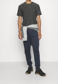 Camiseta de manga corta a rayas negras con pequeño logo; sudadera gris atada a la cintura; pantalones deportivos azul marino; zapatos negros con suela de goma.
