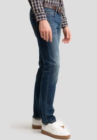 Jeans in denim di colore blu scuro, slim fit, con una finitura sbiadita e cinque tasche. Abbinati a sneaker bianche con dettagli marroni.