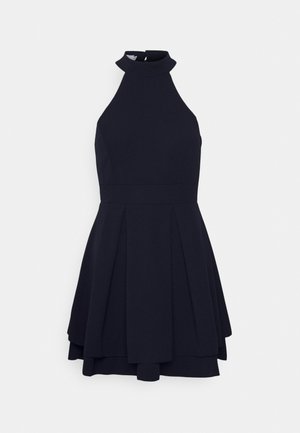 Robe noire sans manches avec un col montant, une taille cintrée et une jupe plissée à plusieurs couches, présentée sur un fond blanc.