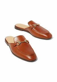 Mocasines de cuero marrón sin respaldo con detalle en forma de herradura de metal dorado en la parte superior, suela plana negra y plantilla acolchada color marrón.