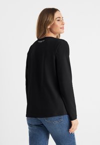 Zwarte lange mouwen shirt met een ronde hals, soepele textuur en subtiele logodetail op de achterkant, gecombineerd met blauwe denim jeans.
