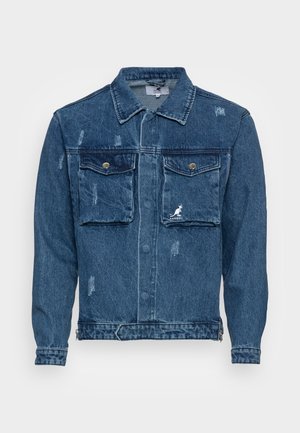 Chaqueta vaquera azul oscuro con bolsillos de solapa abotonados en el pecho, desgaste sutil y un pequeño logo blanco de Kangol en el bolsillo derecho.