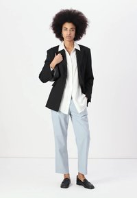 Črn blazer nad belo srajco, svetlo modre hlače in črne čevlje. Blazer ima strukturirano zasnovo in ostre reverje. Liki so voluminozni.